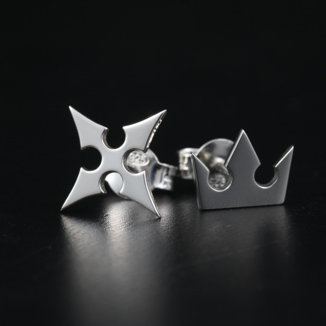 Full view of Korona stud earrings in sterling silver with crown and cross symbols representing light and darkness